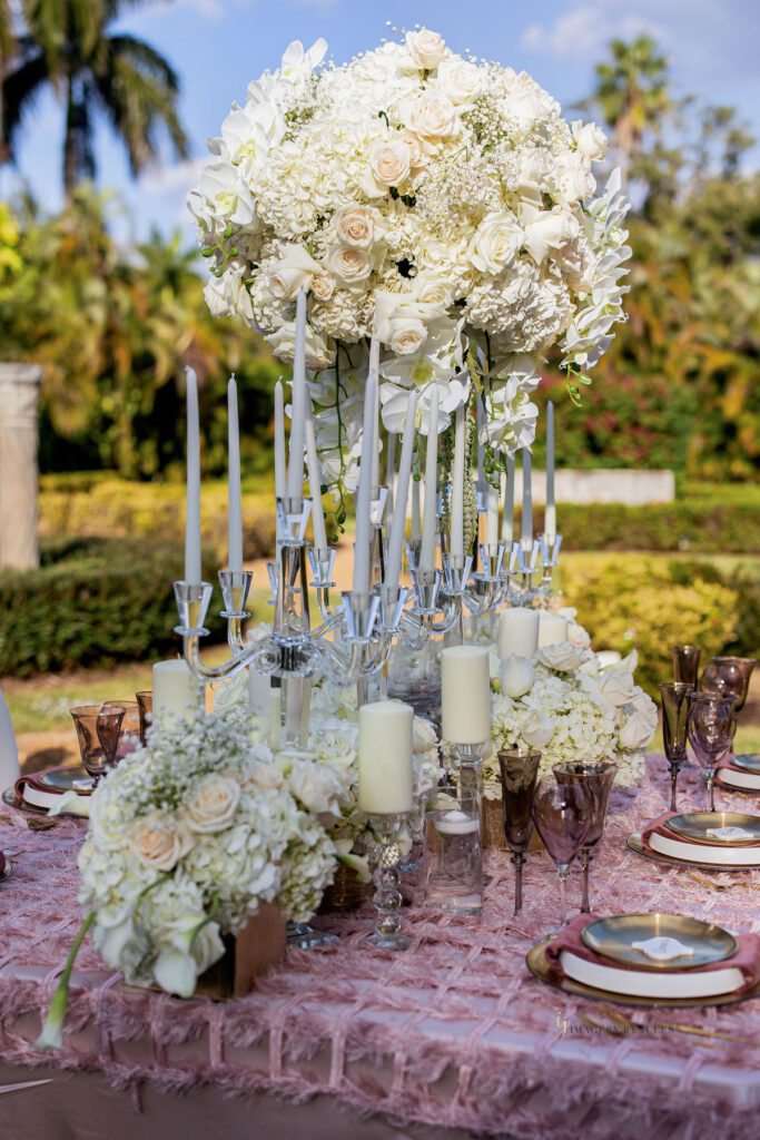 White candles with white and pastel floral arrangements for blooming spring wedding themed tablescape design.