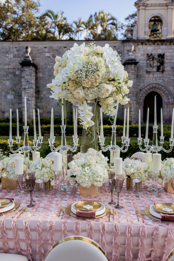 White candles with white and pastel floral arrangements for blooming spring wedding themed tablescape design.